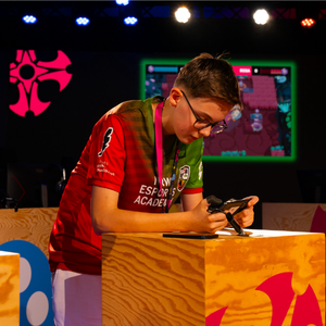 Ein junge spielt Brawl Stars auf einem Handy - dieses hält er quer in der Hand. Er lehnt auf einem Podest bzw. Stehtisch. Das Bild steht repräsentativ für die Telekom eAcademy, da die eAcademy in einem offline Finale mündet.