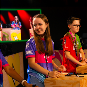 Ein Mädchen spielt Brawl Stars auf einem Handy - dieses hält sie quer in der Hand. Sie lehnt auf einem Podest bzw. Stehtisch. Das Bild steht repräsentativ für die Telekom eAcademy, da die eAcademy in einem offline Finale mündet.