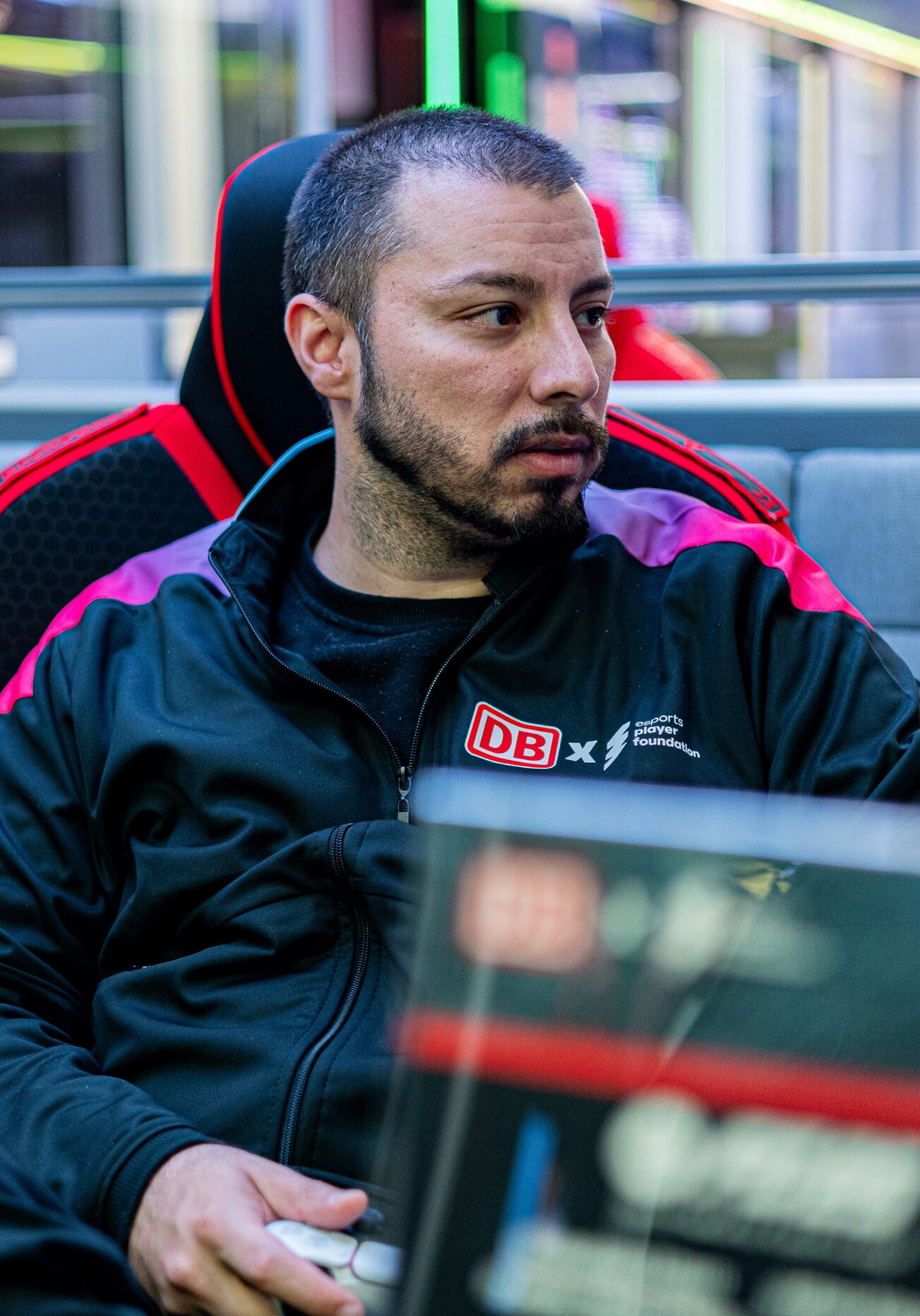 Hakan Aslan Head of EAFC & EA FC Coach. Er hält einen Controller in der Hand, schaut seitlich auf einen Monitor und sitzt auf einem Gaming Chair