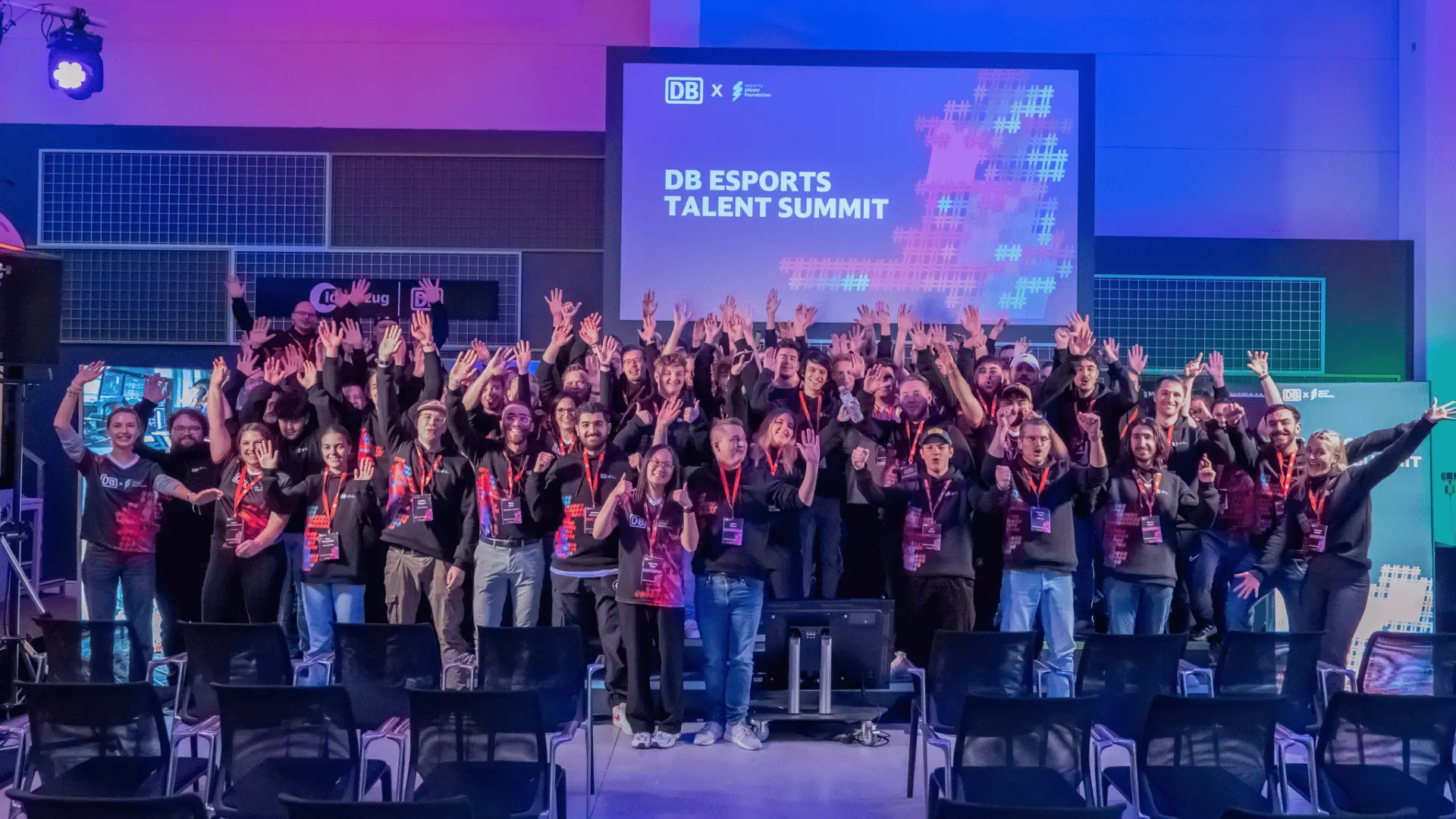 DB Esports-Stipendium Spieler in DB Esports Trikots beim DB Esports Summit im DB Frankfurt Ideenzug Zentrum. Die Gruppe von jungen Talenten steht zusammen und lächelt vor einer modernen, innovativen Hintergrundkulisse, die den Summit und das Zentrum symbolisiert.