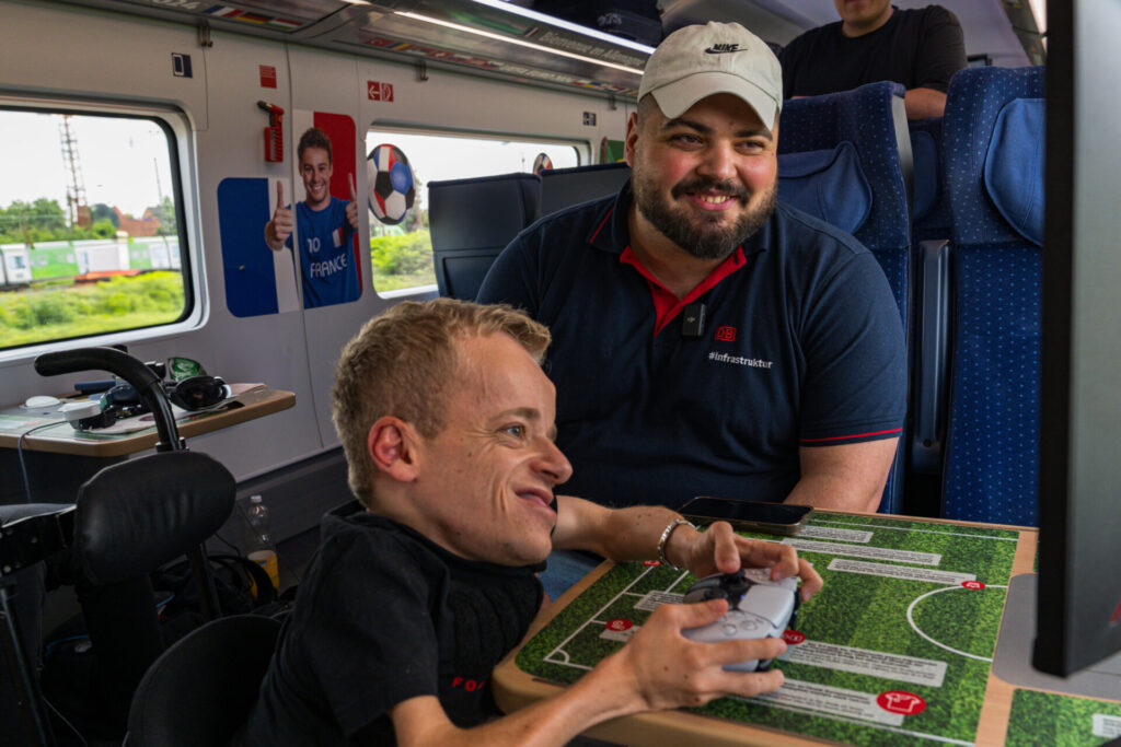 Nik Luginsland, im Rollstuhl sitzen, und Mehmet Mutlu spielen EA FC in einem Zug der deutschen Bahn