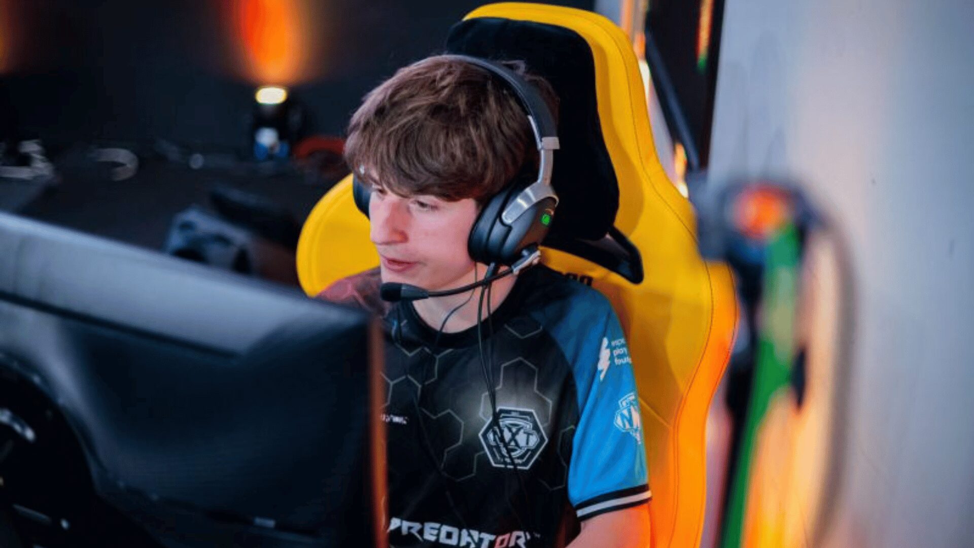 Robert van Treeck, Esports Spieler im Counter-Strike-2 Esports Team XPERION NXT sitzt in einem gelben Gaming Chair vor einem PC. Robert van Treeck, besser bekannt als Rhyzar trägt das XPERION NXT Trikot mit dem Logo der esports player foundation und anderer Marken.